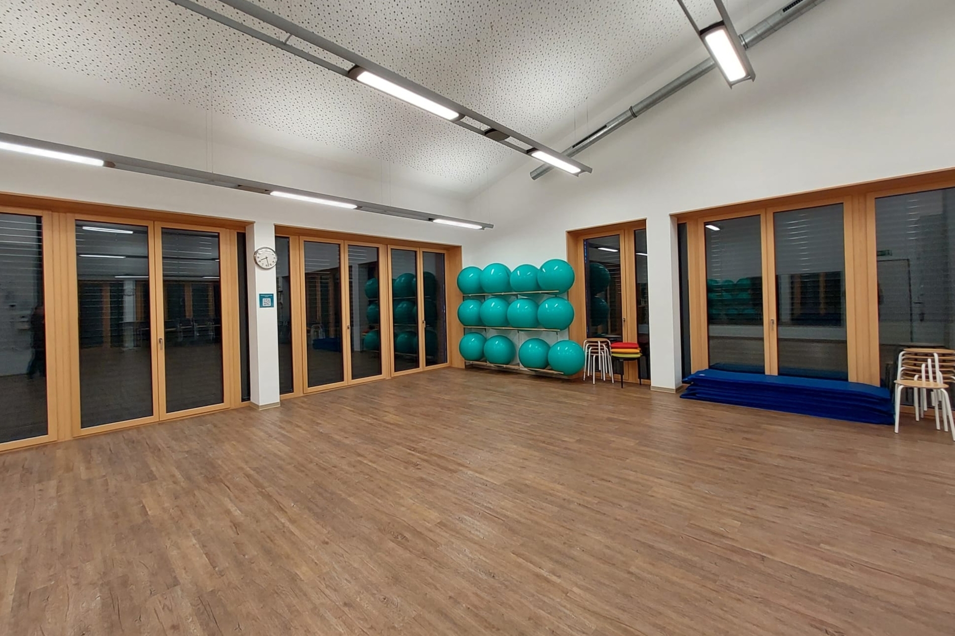 Leerer Kursraum nachts mit aufgeräumten Fitnessbällen, Hockern und Matten an der Seite