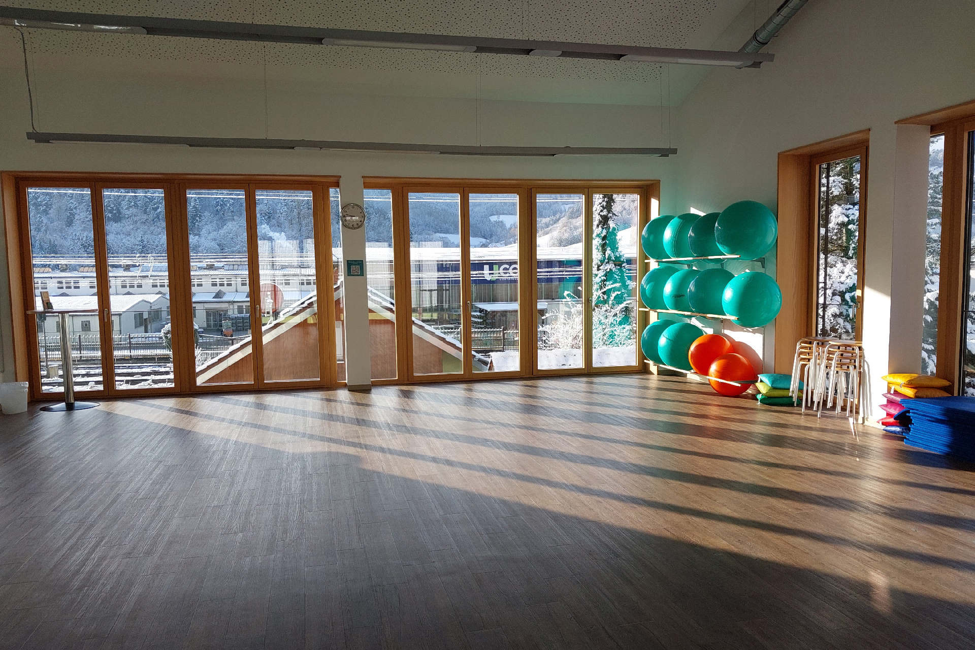 Leerer Kursraum tagsüber mit aufgeräumten Fitnessbällen, Hockern und Matten auf einer Seite