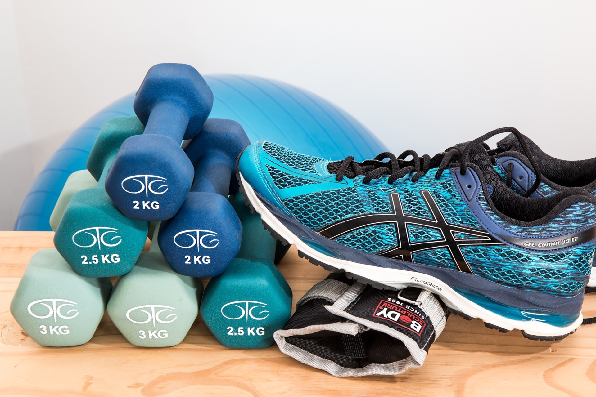 Fitnessausrüstung: Hanteln, Gewichtsmanschette und Sportschuh vor einem Fitnessball
